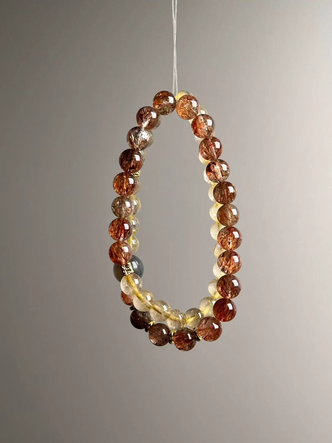 Angle view — lustrous Golden Rutile rounds paired with Black-Gold Super Seven; gray moonstone shows soft blue flash.
