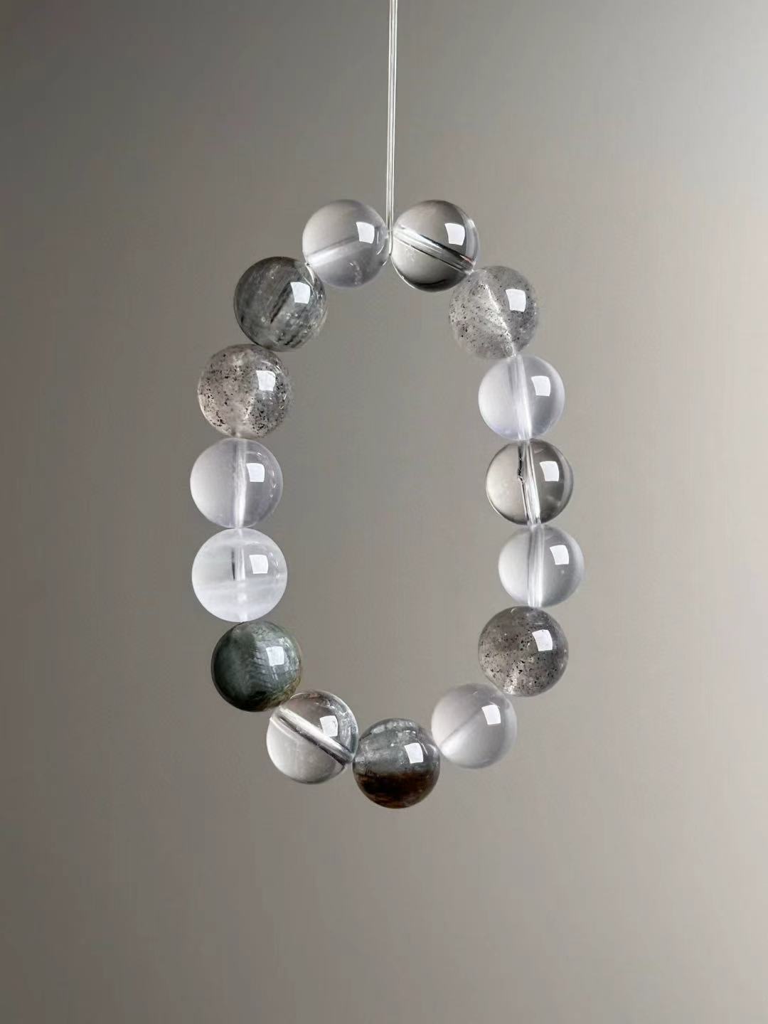 Suspended front view showing clear quartz, milky quartz, amphibole hair quartz and white phantom beads in a cool grey palette.