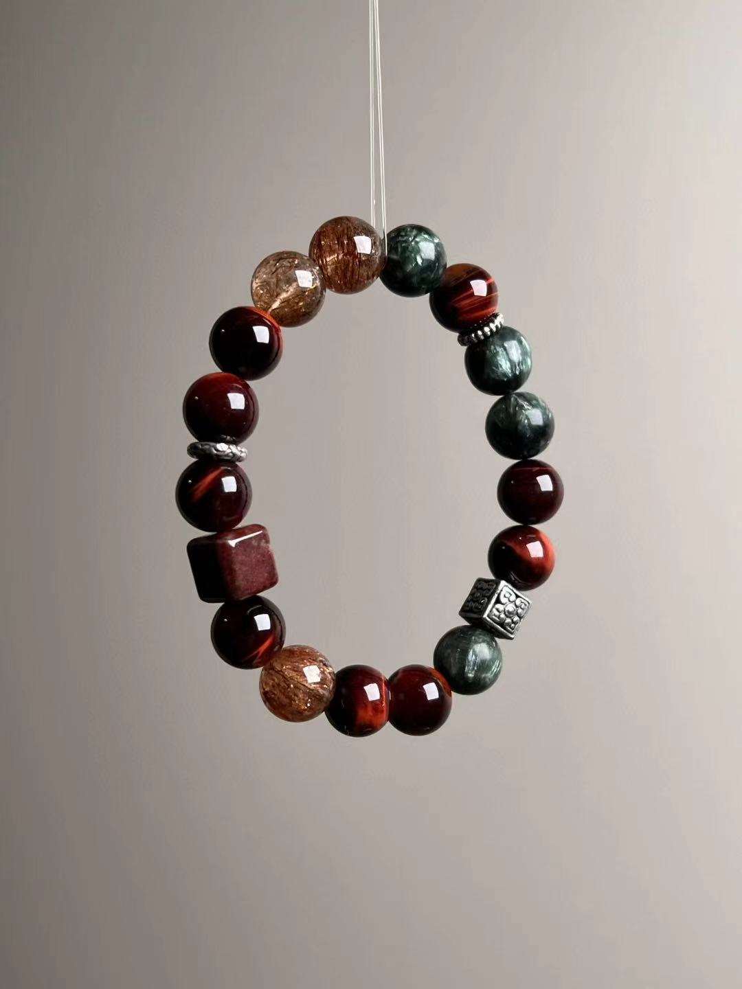 Front loop view highlighting chatoyant red tiger’s eye rounds with golden-rutile Super Seven and deep green seraphinite.