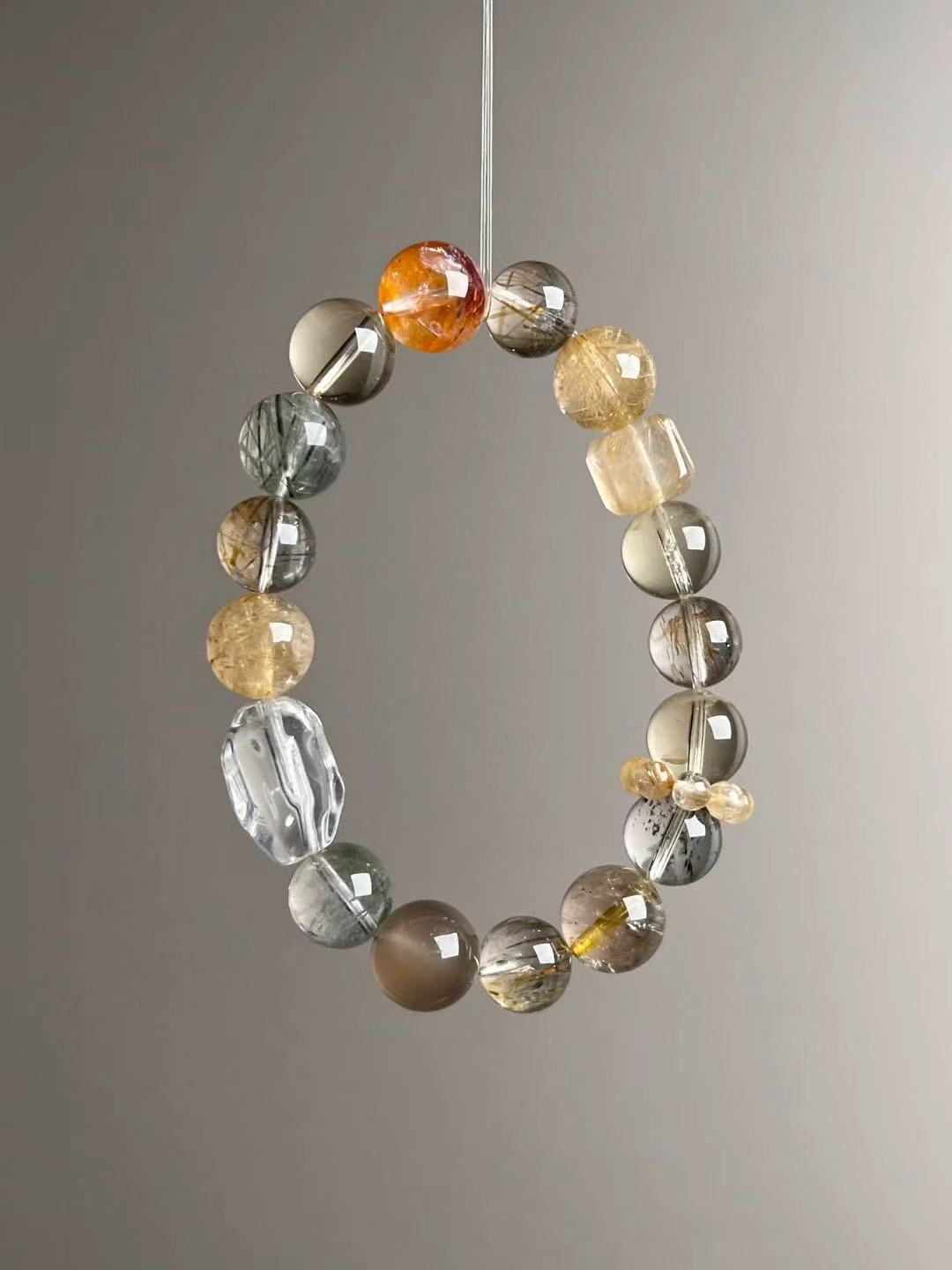Angled hero—shows rutile needles, green phantom inclusions and smoky-grey sunstone tones on the 12–10.5 mm bracelet