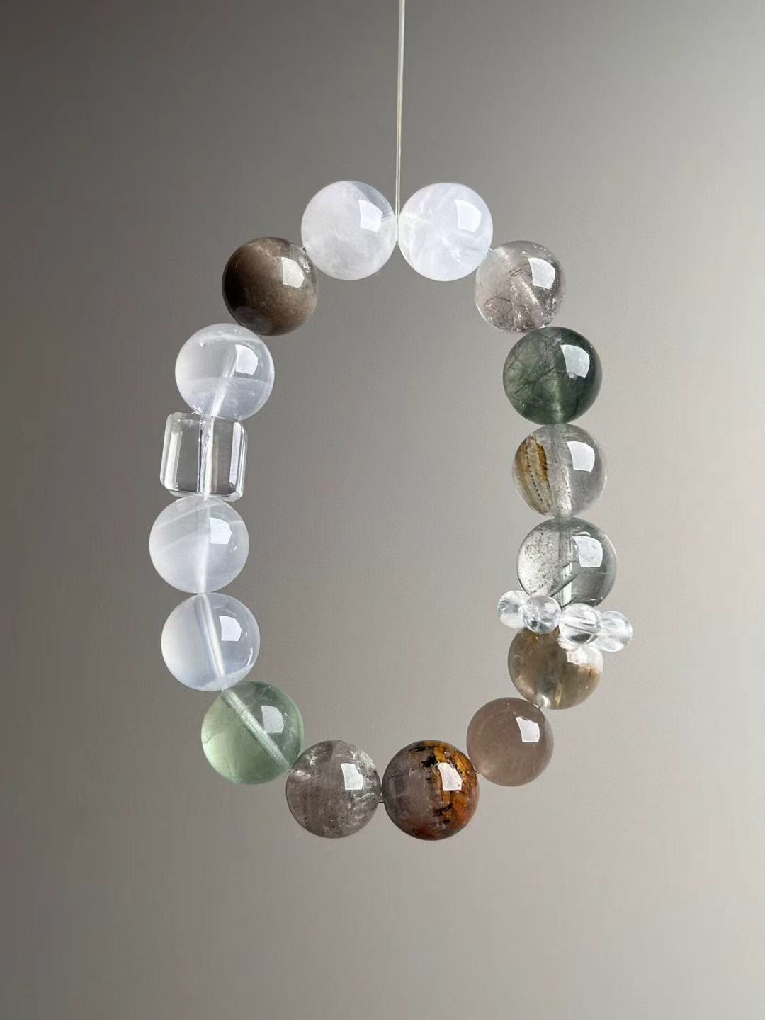 Suspended loop showing icy clarity and balance; clear-quartz cube focal with white/mossy inclusions.