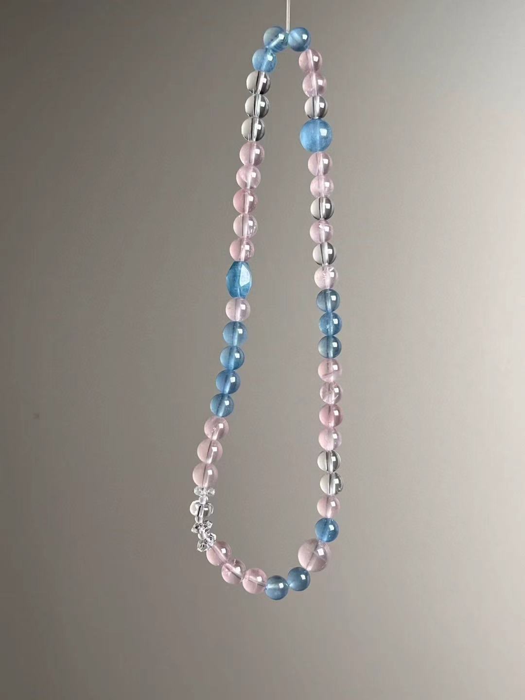 Angle shot featuring the faceted aquamarine bead and the even rhythm of translucent rose quartz and clear quartz.