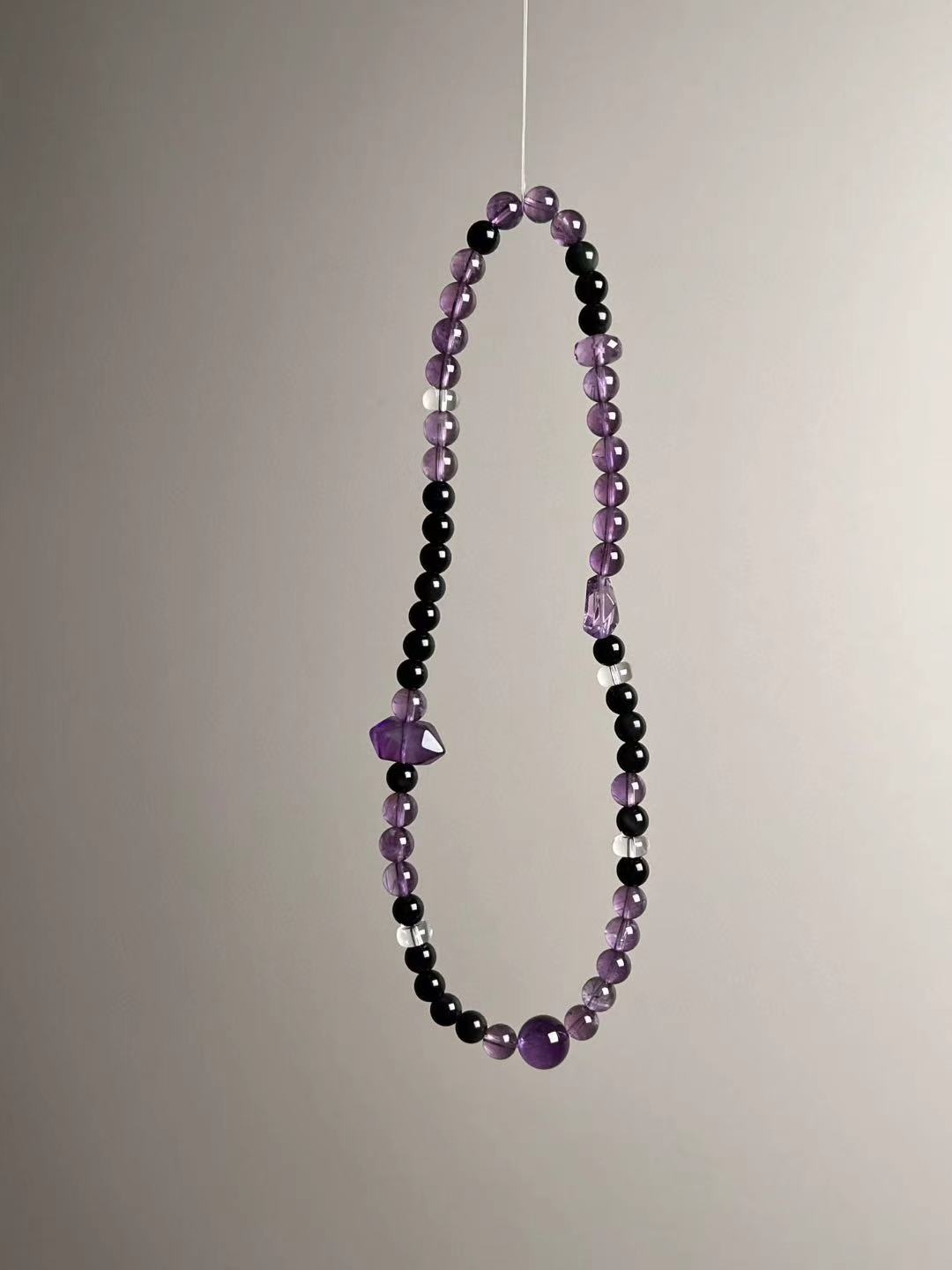 Angle shot highlighting faceted double-terminated amethyst focal beside obsidian and translucent amethyst rounds