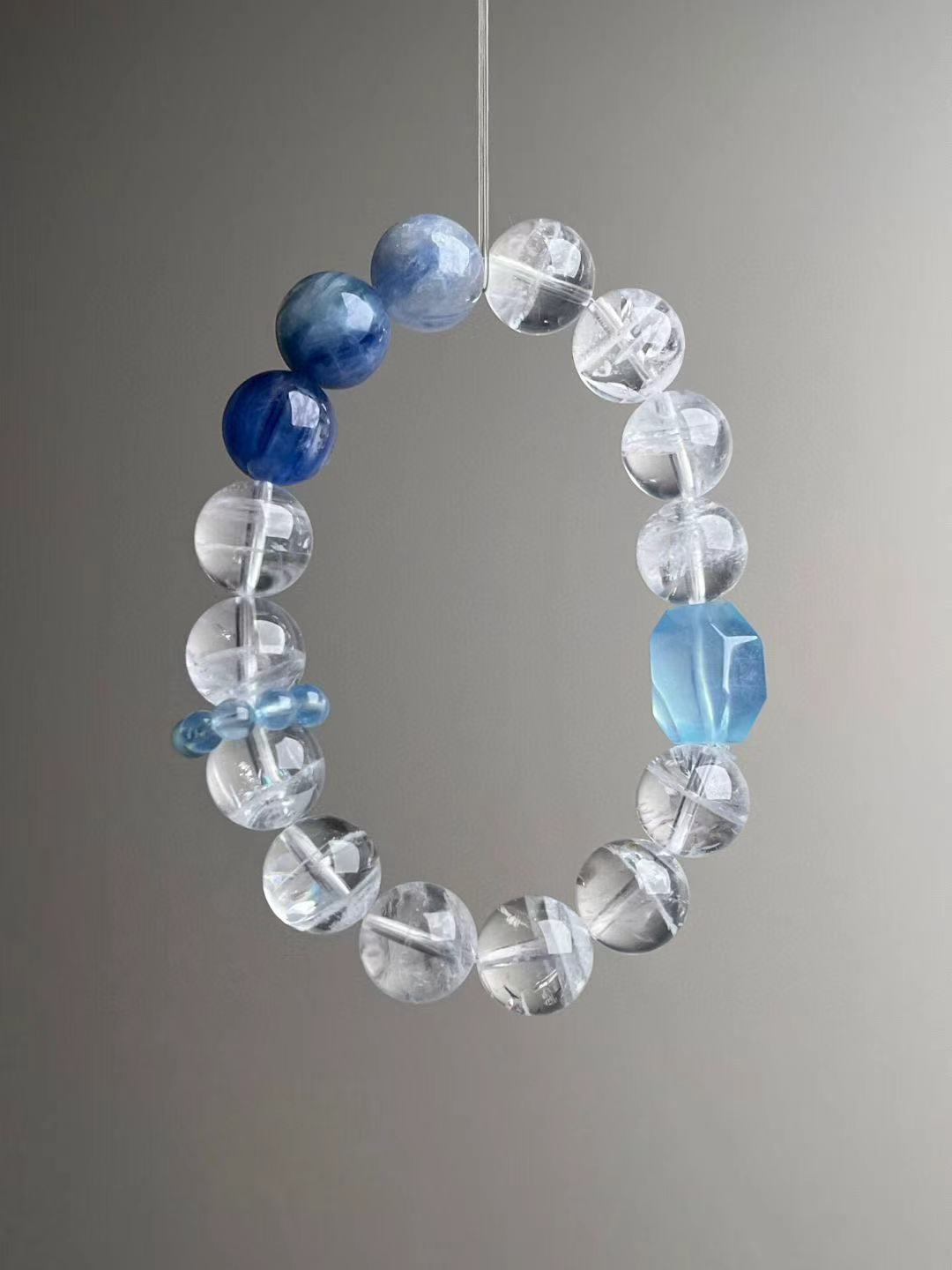 Reverse angle showing gradient from transparent quartz to denim-blue kyanite; faceted aquamarine focal bead.
