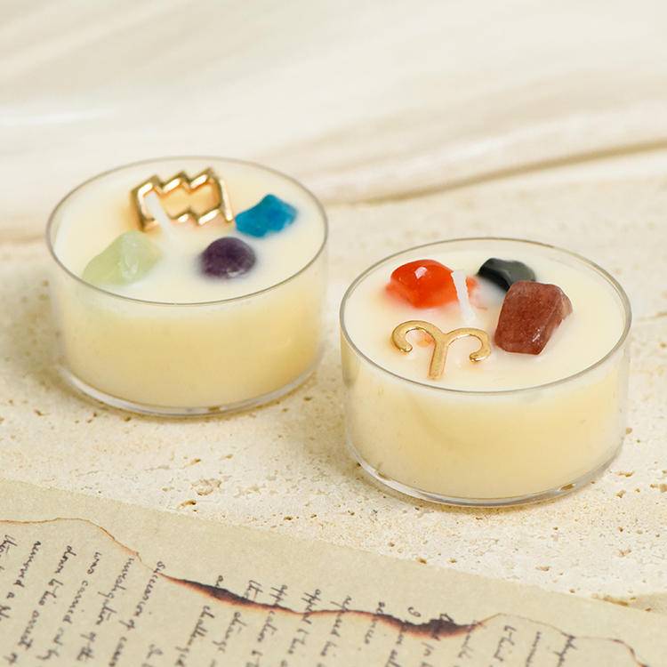 two zodiac gemstone tea-light candles side by side showing different sign charms and crystals.