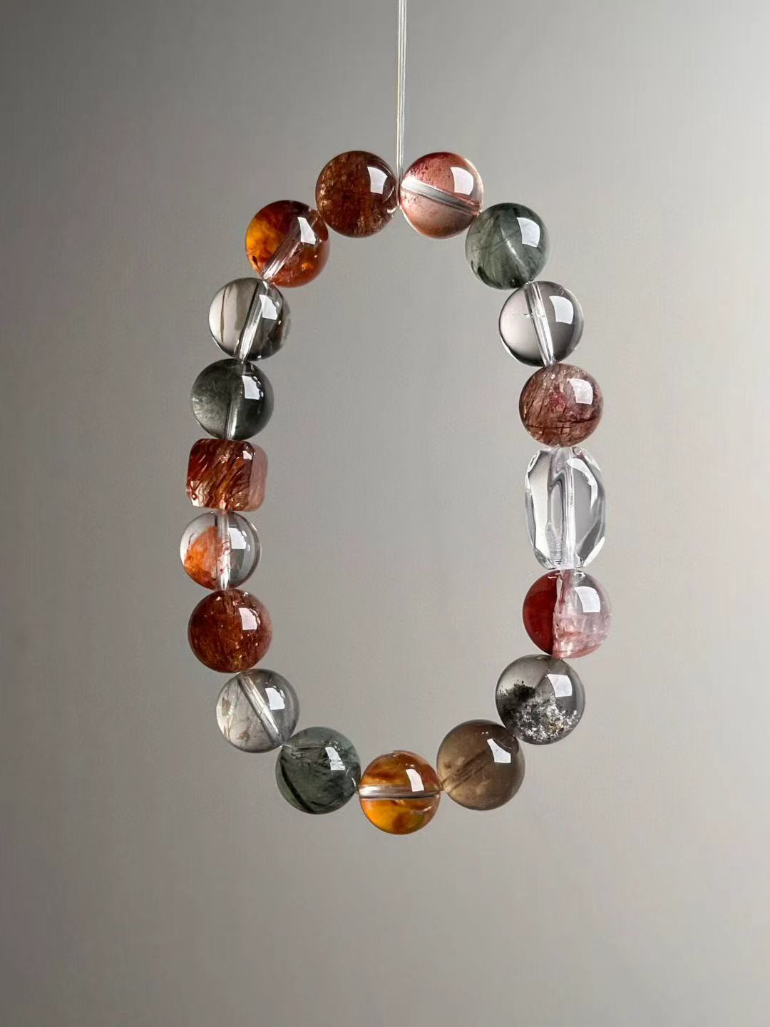 Suspended loop view showing even bead gradation and icy transparency with warm reds and forest greens; faceted clear-quartz focal visible.