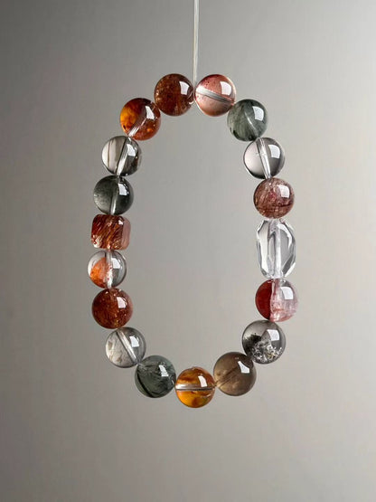 Suspended loop view showing even bead gradation and icy transparency with warm reds and forest greens; faceted clear-quartz focal visible.