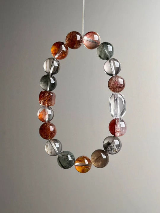 Suspended loop view showing even bead gradation and icy transparency with warm reds and forest greens; faceted clear-quartz focal visible.