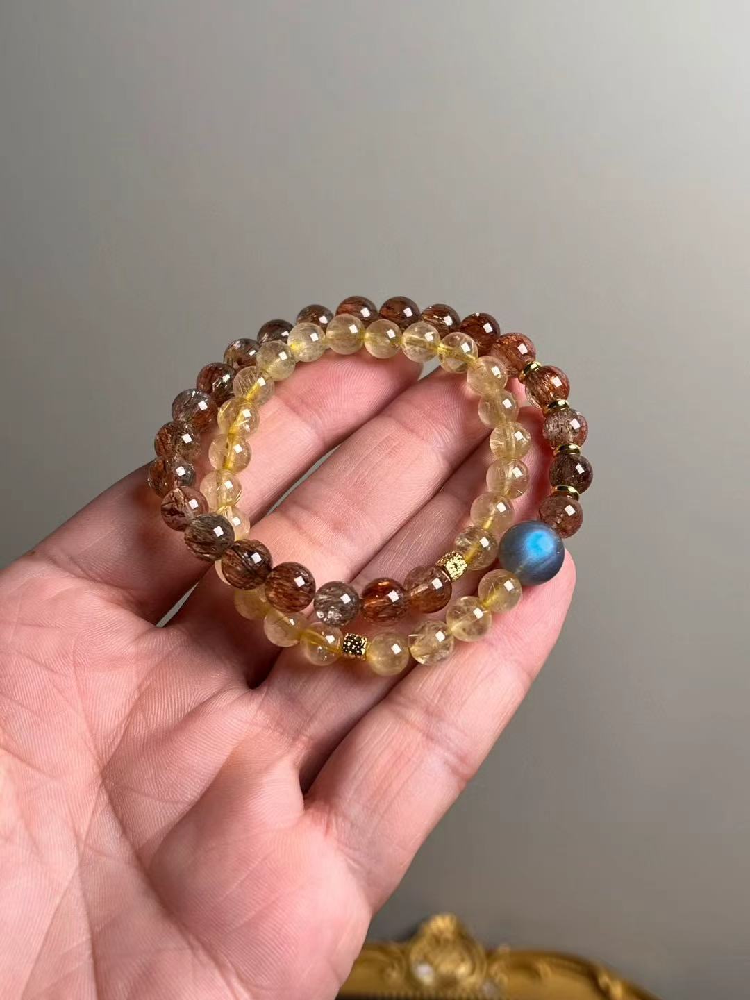 Hero view — double-wrap bracelet of Black-Gold Super Seven and Golden Rutile with a gray moonstone focal bead, approx. 11–7 mm beads.