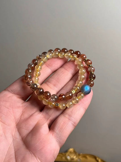 Hero view — double-wrap bracelet of Black-Gold Super Seven and Golden Rutile with a gray moonstone focal bead, approx. 11–7 mm beads.