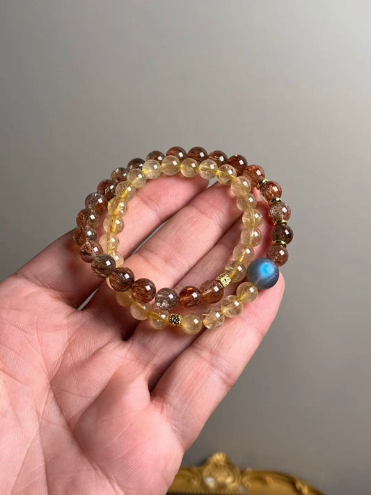 Hero view — double-wrap bracelet of Black-Gold Super Seven and Golden Rutile with a gray moonstone focal bead, approx. 11–7 mm beads.