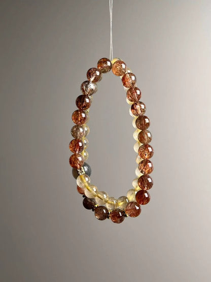 Angle view — lustrous Golden Rutile rounds paired with Black-Gold Super Seven; gray moonstone shows soft blue flash.