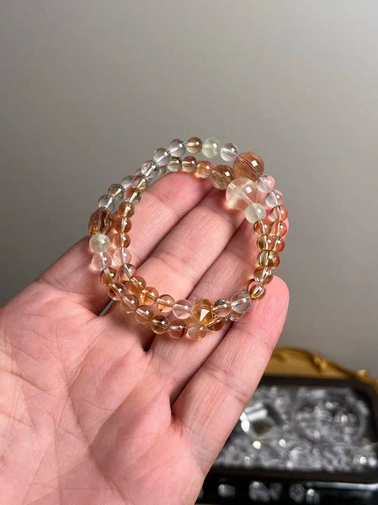Angle view — slim triple-wrap with Clear Quartz rounds, golden rutile highlights and Orange Phantom focal bead.