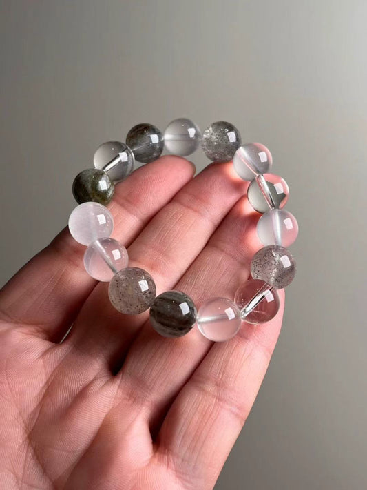 Hand shot of Aurora Cleanse bracelet — clear & milky quartz with white/seasonal phantom and amphibole “rainbow hair” inclusions, Signature 13–12 mm.