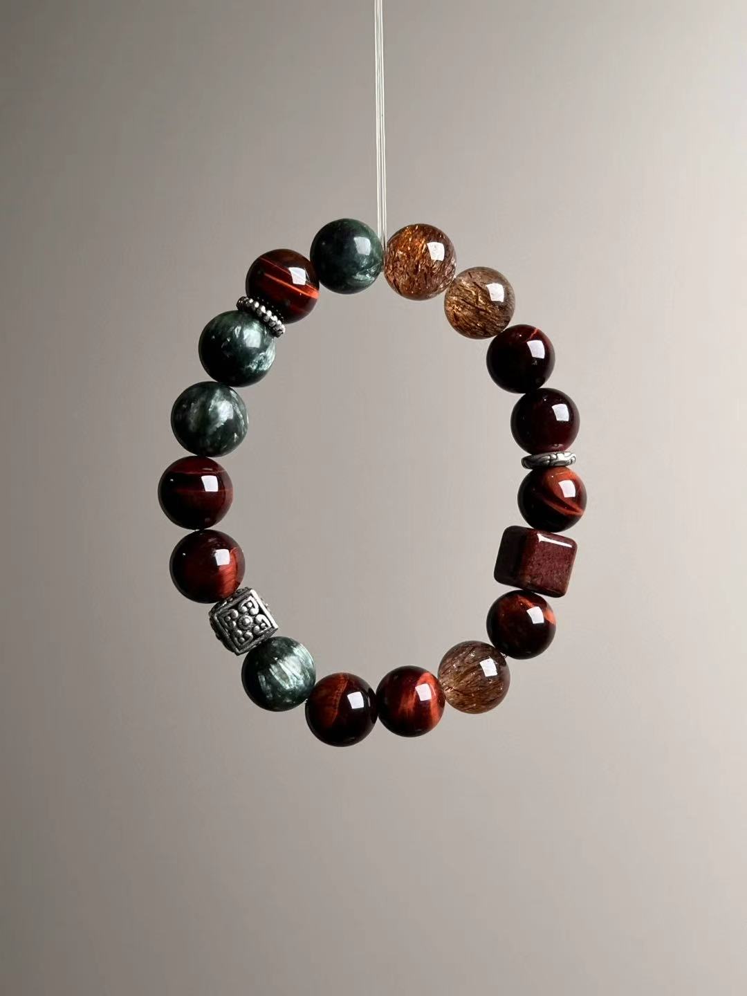 Side view focusing on black-gold Super Seven beads with golden needles beside glossy red tiger’s eye.