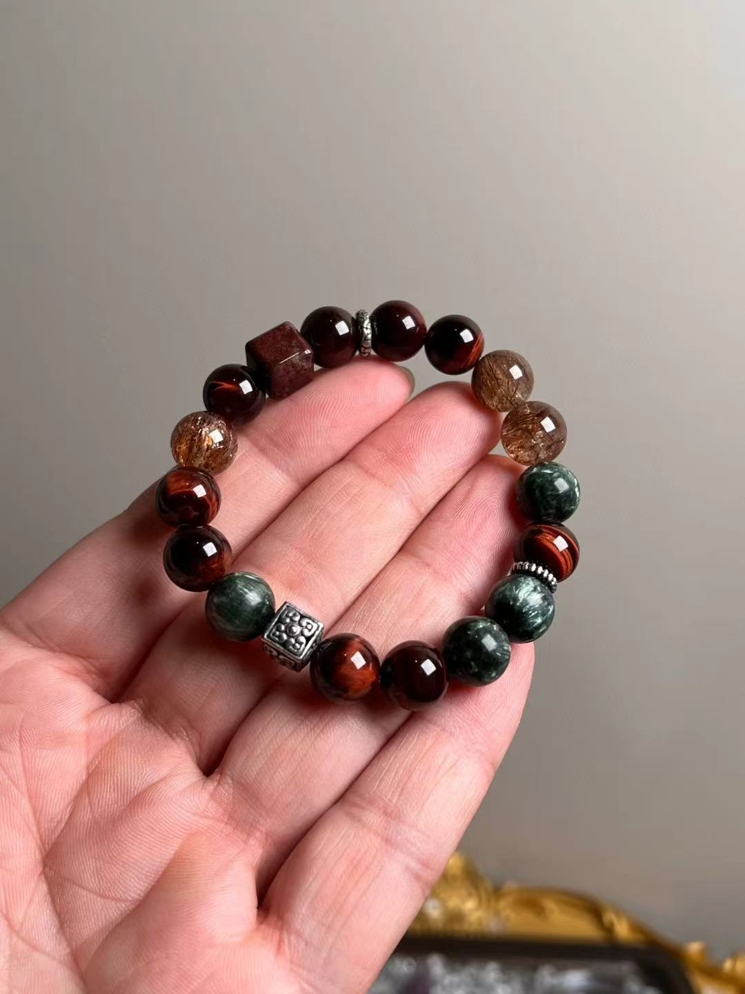 Hand shot of Crimson Accelerator bracelet — red tiger’s eye, black-gold Super Seven, seraphinite (green dragonstone) and phantom quartz, ~10.5 mm.