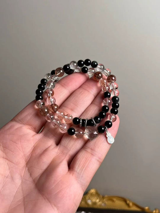 Hand shot of double-wrap bracelet — Black-Gold Super Seven with obsidian accents and sterling silver lucky gourd & fish runner charms (10–6 mm)