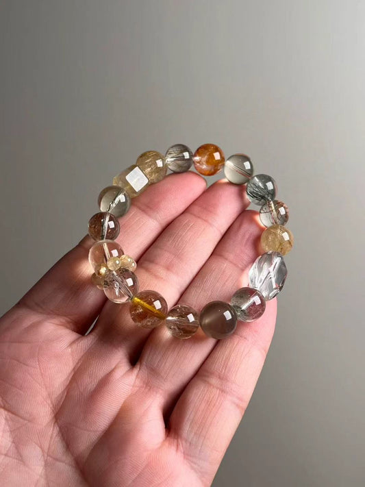 On-hand photo—12–10.5 mm Gold Rutilated Quartz, White Phantom, Black-Gold Super Seven, Green Phantom, Grey Sunstone & Clear Quartz bracelet with yellow bead-cluster spacer