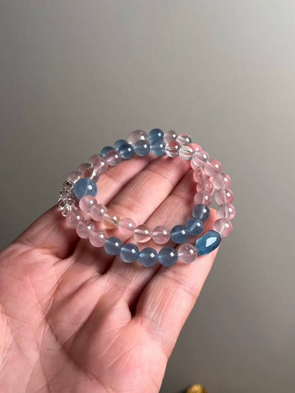 Hand shot of Serene Voice double-wrap — aquamarine, rose quartz and clear quartz with a faceted aquamarine focal (approx. 10.5–7.5 mm).