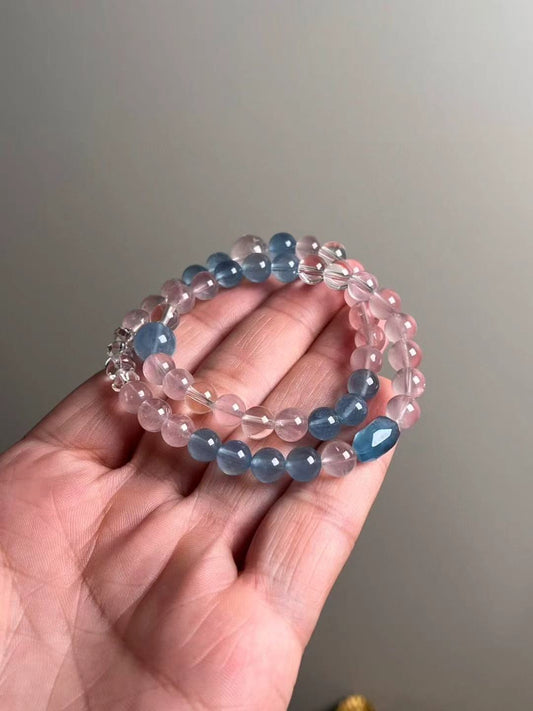 Hand shot of Serene Voice double-wrap — aquamarine, rose quartz and clear quartz with a faceted aquamarine focal (approx. 10.5–7.5 mm).