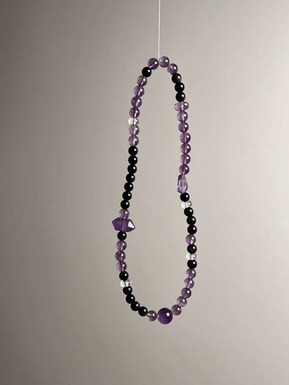 Angle shot highlighting faceted double-terminated amethyst focal beside obsidian and translucent amethyst rounds