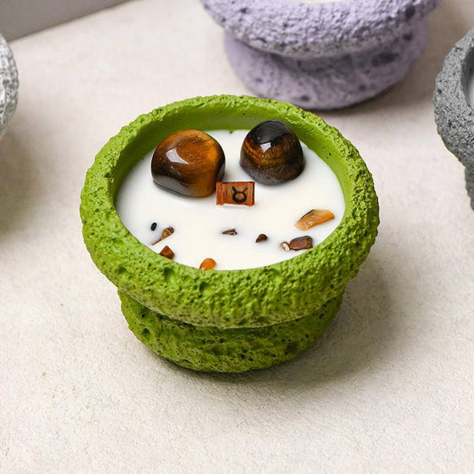 aurus candle close-up in green vessel with tiger’s eye stones and wooden wick symbol tag.