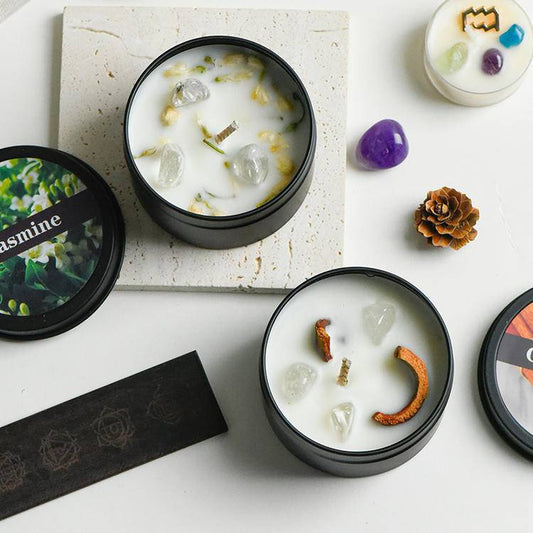 Collection grid of crystal-infused aromatherapy tin candles with black travel tins and botanical garnishes.