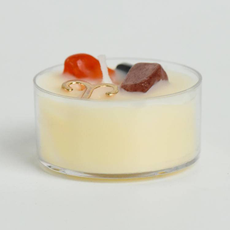 Macro detail of zodiac tea-light candles highlighting gold sign charms and gemstones embedded in wax.